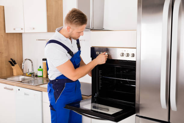 Young Male Technician In Overall Checking Oven In Kitchen